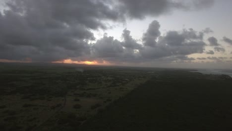 vista aérea de los bosques de la isla de mauricio, campos agrícolas y colinas contra el cielo al atardecer y las nubes rosadas.