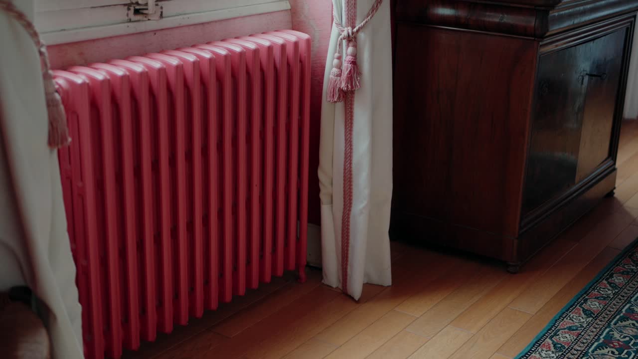 Pink radiator by a curtained window in a cozy room