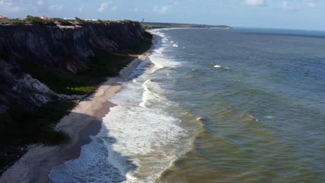 Tilt-up-aerial-drone-shot-of-huge-beautiful-white-cliffs-on-the-coast-in-the-tropical-state-of-Paraiba,-Brazil-near-the-beach-capital-of-Brazil-on-a-warm-sunny-summer-day-with-small-waves