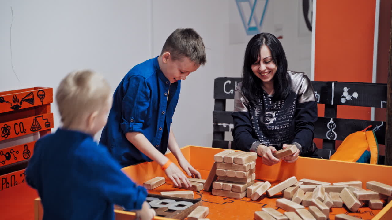 Happy boys and mother playing wooden tower table game together. Jenga falls on the table. The tower falls.