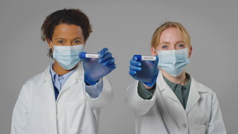 fotografía de estudio de trabajadores de investigación de laboratorio con máscaras faciales sosteniendo tubos de ensayo etiquetados con omicron y covid-19