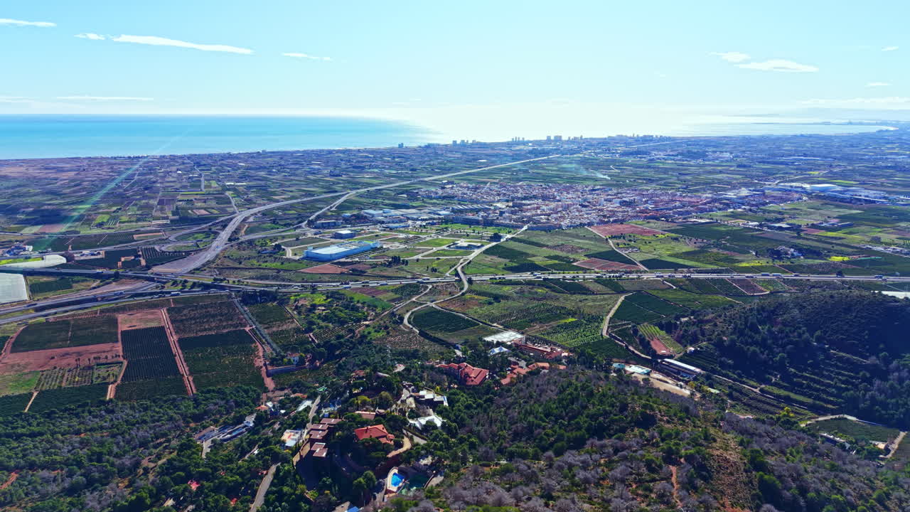 Vista dall'alto che mostra terreni agricoli, costa e città in lontananza in una giornata soleggiata.