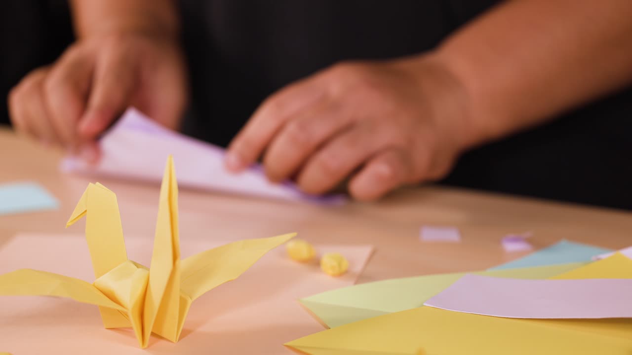 Primo piano di mani che piegano con cura della carta bianca per creare figure di origami su una scrivania di legno