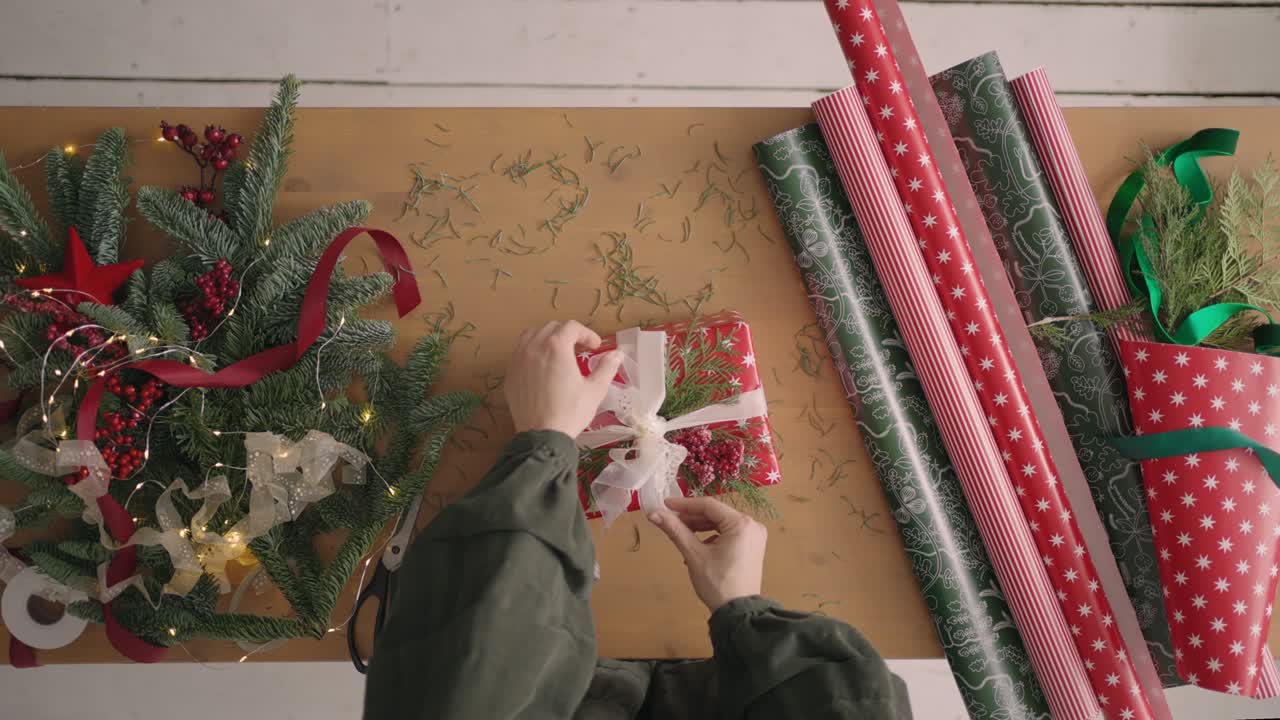 하향식 계획: 한 여성이 선물을 포장하기 위해 테이블 위에 놓고 그 위에 선물 리본을 조입니다. 장식가와 선물 포장 테이블