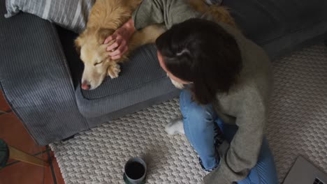 smiling caucasian woman stroking her pet dog on sofa next to her