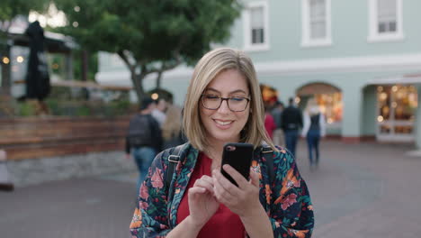 Porträt-Einer-Hübschen-Blonden-Frau,-Die-Mit-Einer-Brille-Im-Städtischen-Hintergrund-SMS-Schreibt-Und-über-Die-Social-Media-App-Ihres-Smartphones-Surft