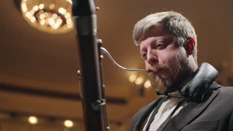 handsome man is playing bassoon on scene of opera house or philharmonic hall closeup portrait