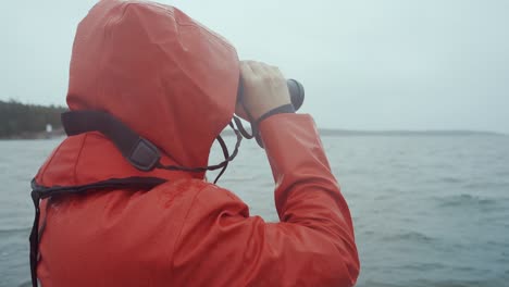 man in red raincoat looking trough binoculars in storm