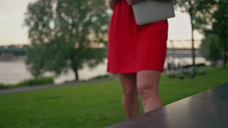 hermosa mujer vestida de rojo con una laptop caminando hacia el banco en el parque y sentada en ella