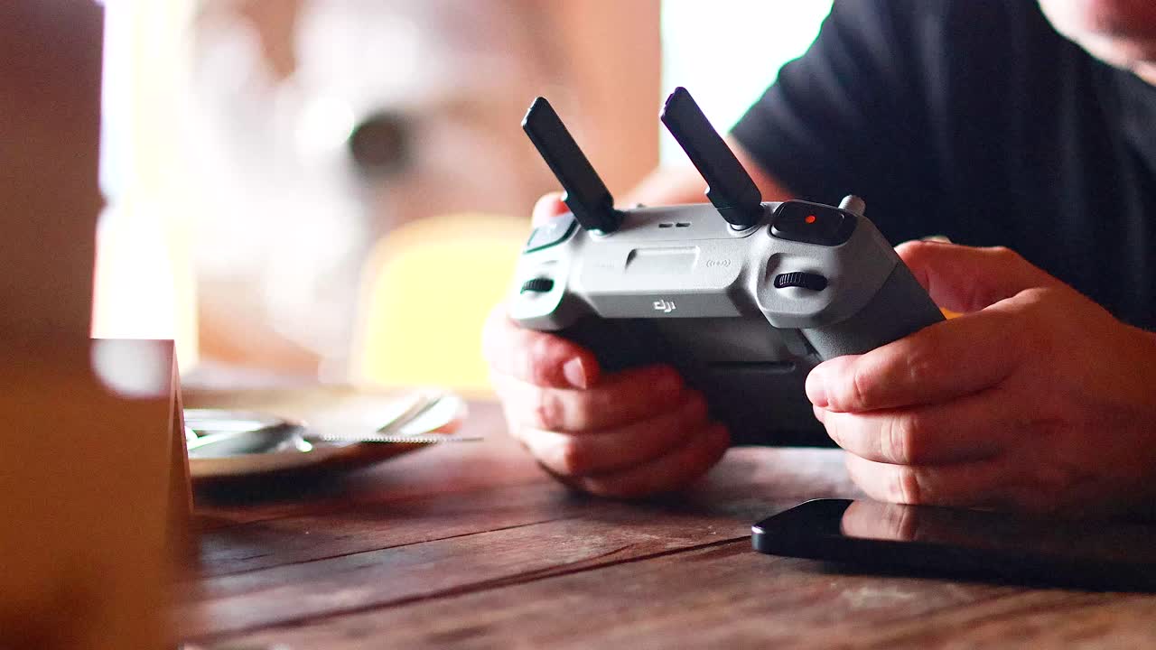 Hands operating a drone controller on a wooden table indoors. Warm lighting creates a cozy atmosphere in Phuket, Thailand