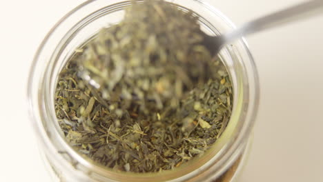 spoon-is-taking-out-a-pile-of-green-tea-leaves-out-of-a-glass-jar-in-100-FPS