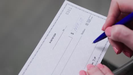 business woman hand signs and filling bank check for one thousand 1000 dollars