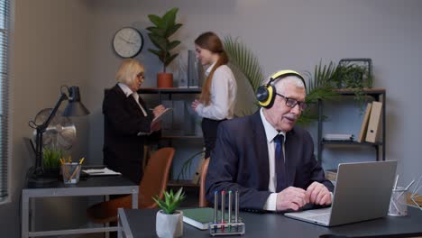 Alegre-Hombre-De-Negocios-Senior-Trabajando-En-Una-Computadora-Portátil-Sentado-En-El-Escritorio,-Escuchando-Música-Y-Bailando