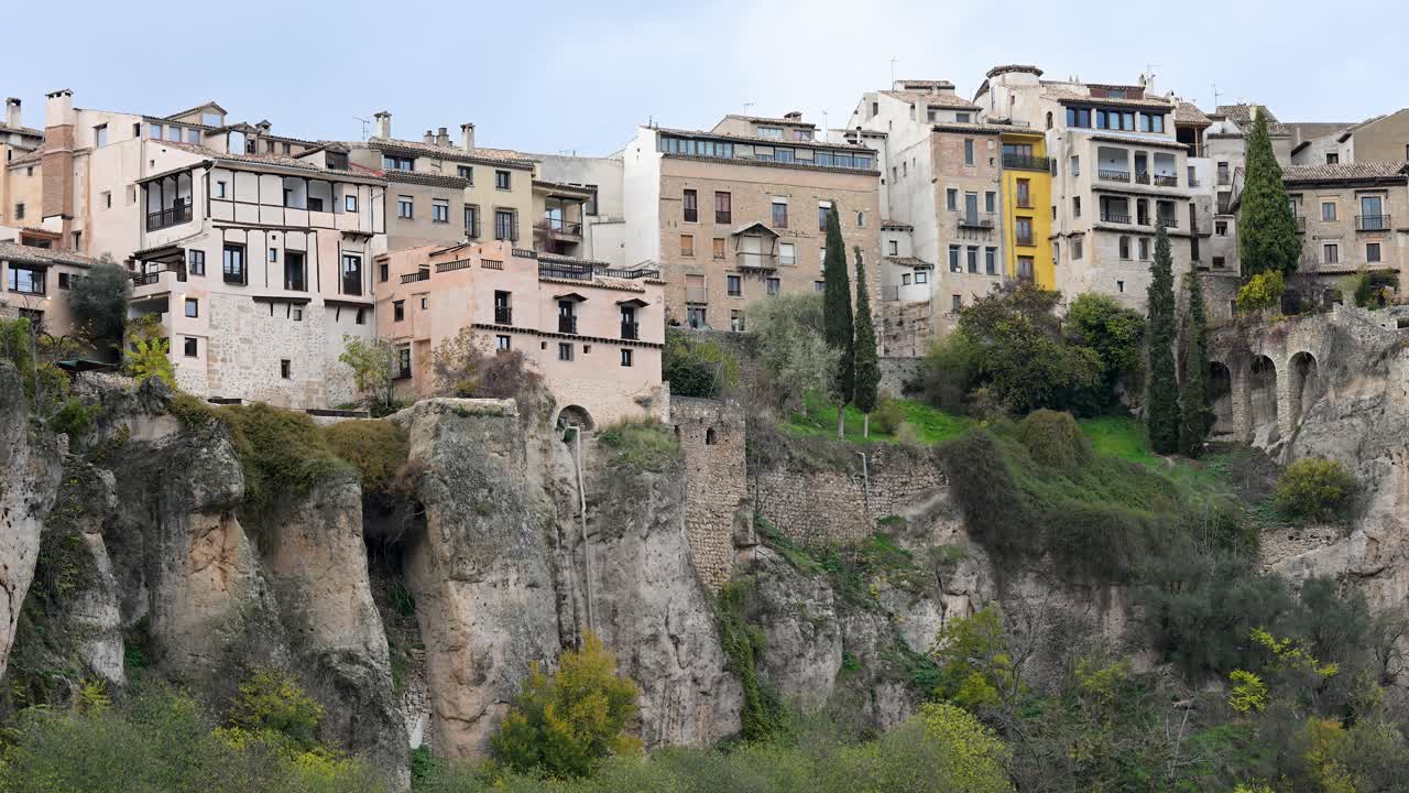A scenic view of Cuenca, Spain, where the historic Hanging Houses (Casas Colgadas) overlook the deep Huecar river gorge on an overcast day.