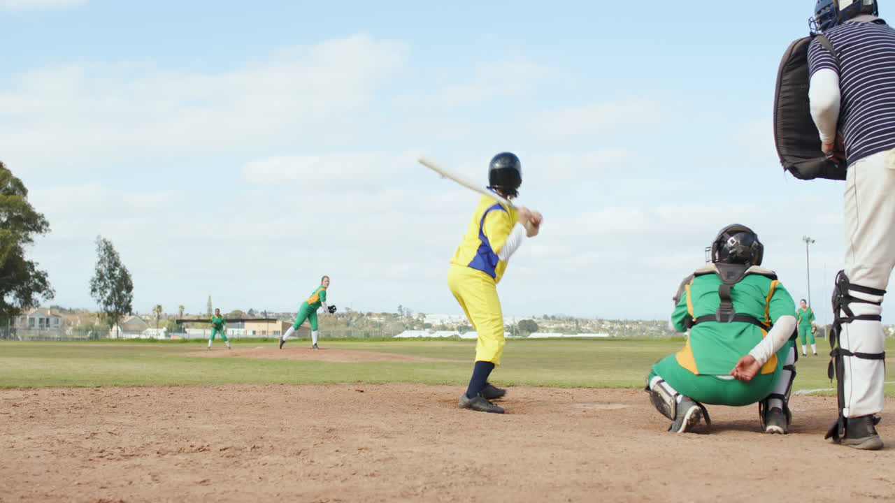 Giocatrici di baseball multietniche e arbitro uomo che battono la palla e corrono su un campo da gioco.