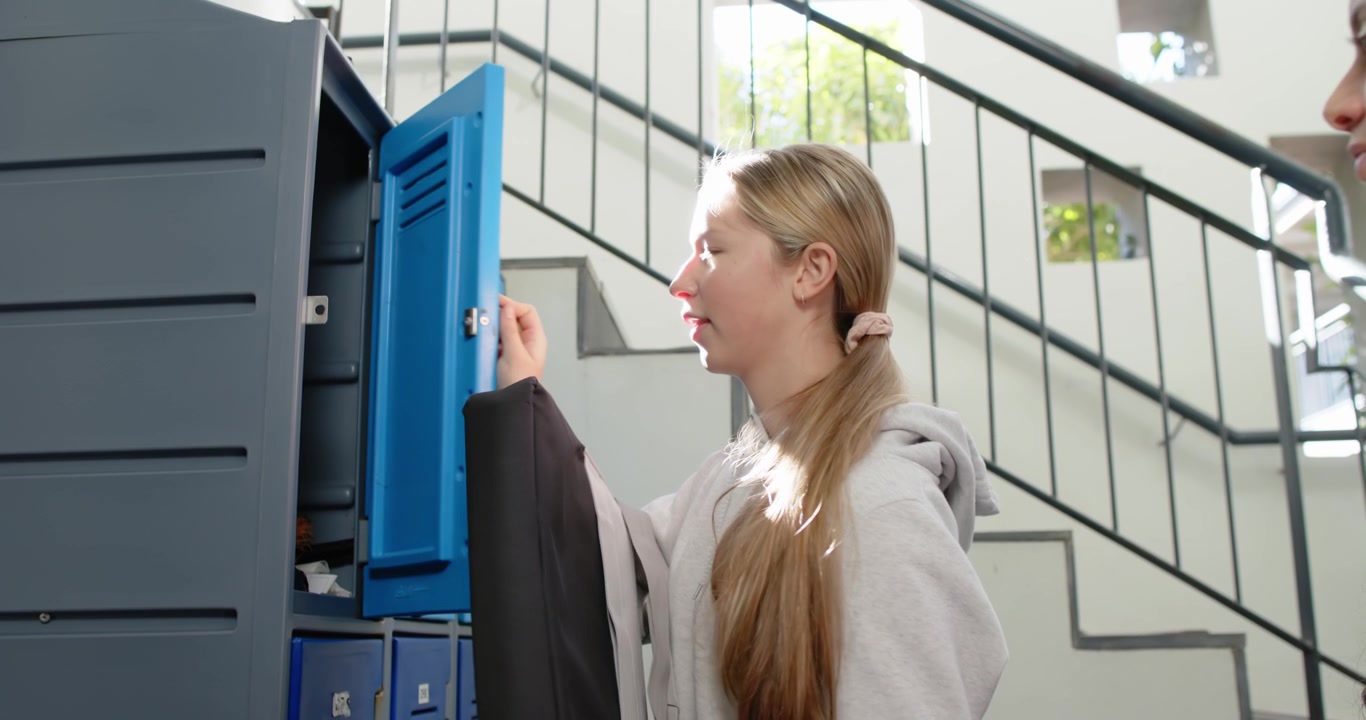 Teenage female friends watching as blonde girl unlocking locker, taking black padded case for class
