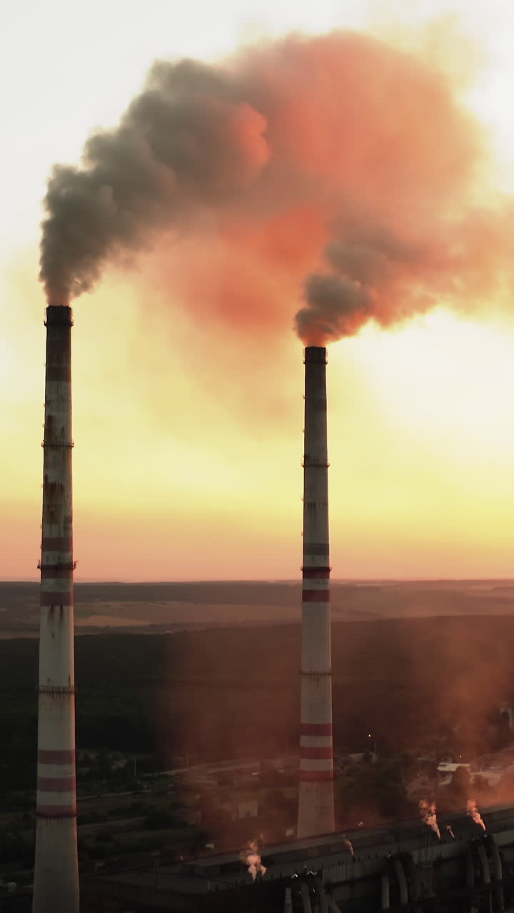 Plant pipes pollute atmosphere. Aerial drone view of high smoke stack. Vertical video