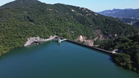 A dynamic aerial shot moving forward while tilting downward towards the dam and control tower of Shing Mun Reservoir in Hong Kong