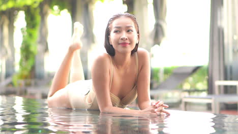 sexy asian woman in a swimsuit lying on infinity pool border and enjoying in spa day, full frame