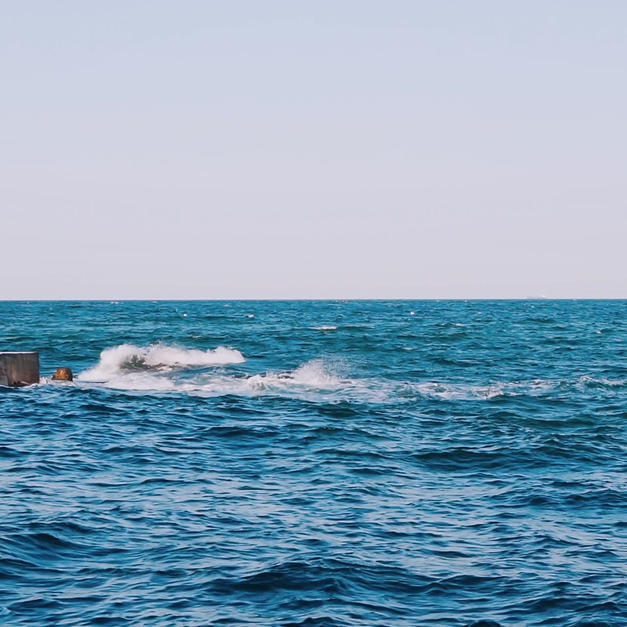 Blue seascape background. Motion of water waves in the sea. Stone dock in seawater. Slow motion.