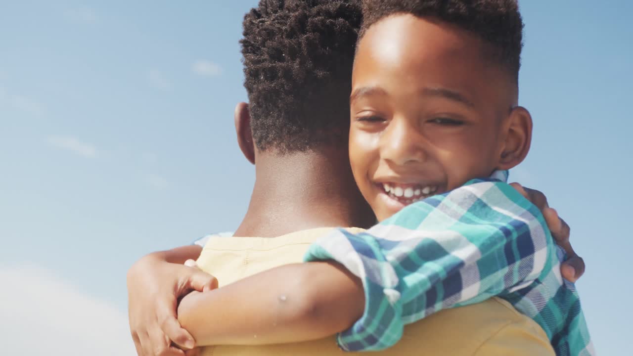 hijo afroamericano sonriendo mientras abrazaba a su padre en la playa