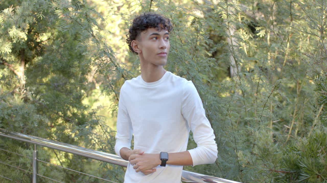 Young man in white shirt standing outdoors, wearing smartwatch, looking away, copy space