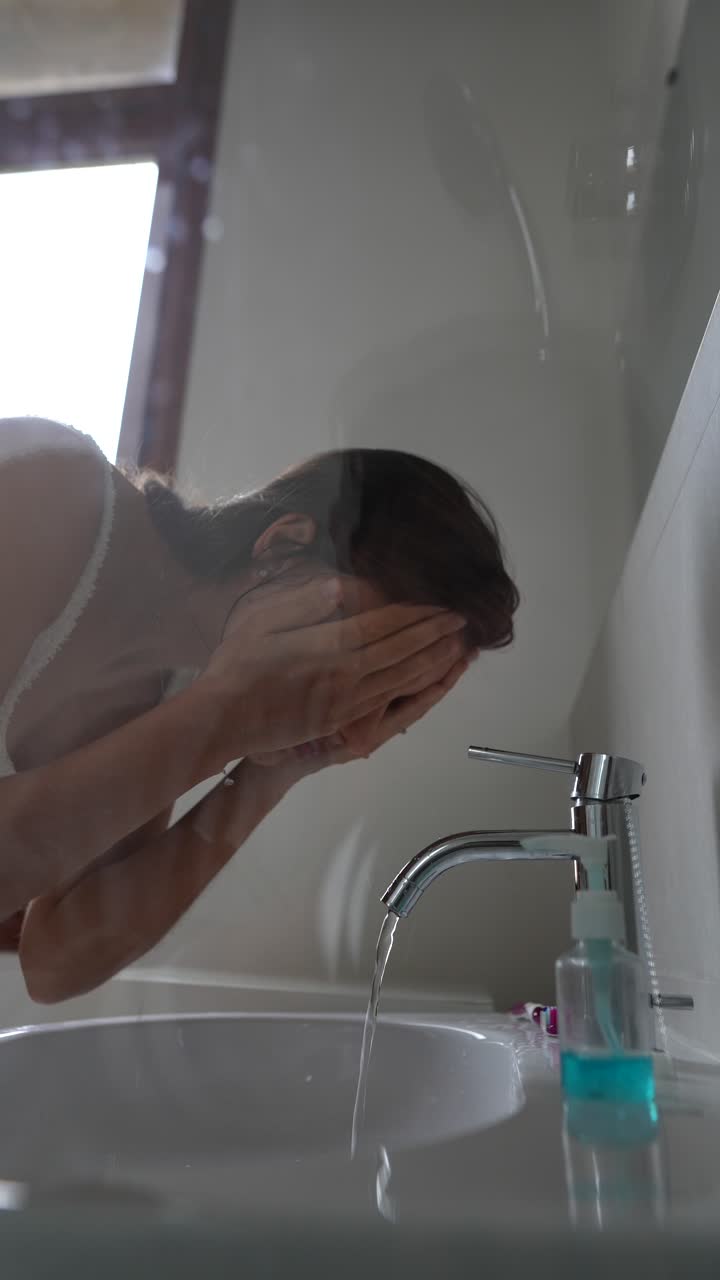 женщина моет лицо в ванной.