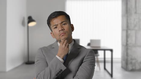 Portrait-Of-Businessman-Wearing-Suit-In-Thought-Standing-In-Modern-Open-Plan-Office