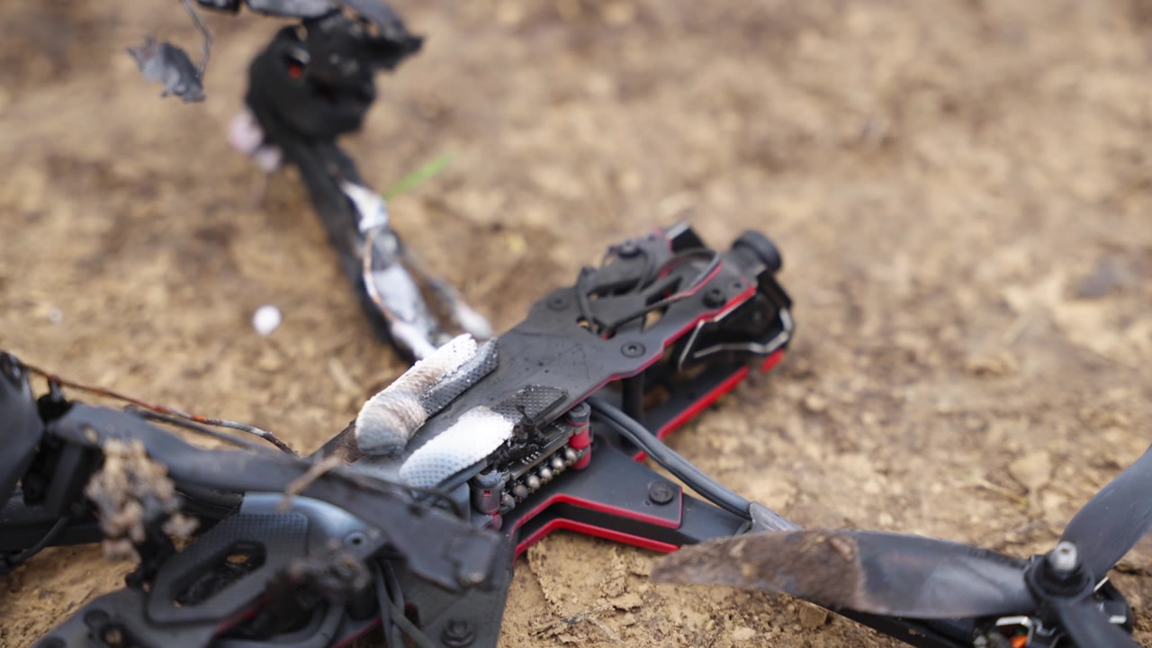 Поврежденный FPV-дрон со сгоревшими компонентами и сломанной конструкцией на грунте на открытом воздухе.