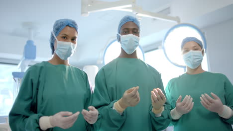 portrait of three diverse male and female surgeons in operating theatre, slow motion