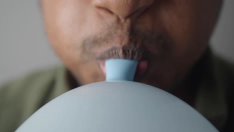 person blowing up a light blue balloon