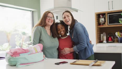 retrato de una feliz pareja de lesbianas caucásicas y su hija afroamericana abrazándose en la cocina