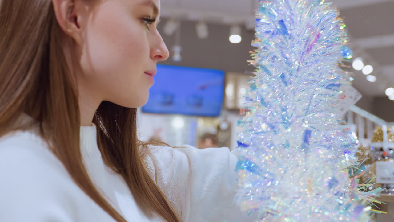 Close-up of lady holding shimmering tinsel in decor store, observing it carefully with bokeh lights in the background and blue screen visible