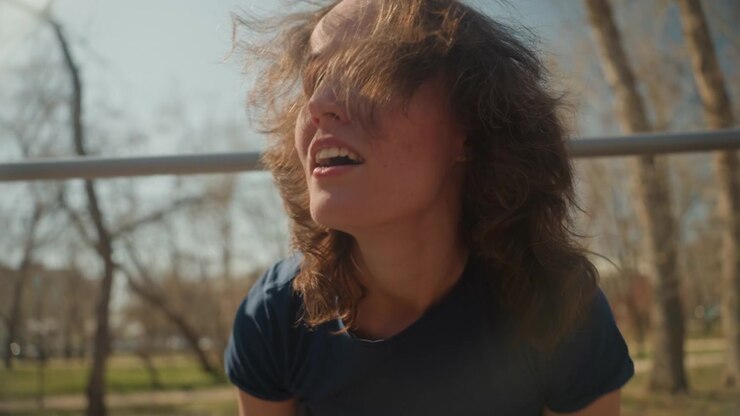 Close up of young woman running towards camera in outdoor park then climbing and interacting with playground equipment. Woman wears casual clothing including jeans and t shirt throughout