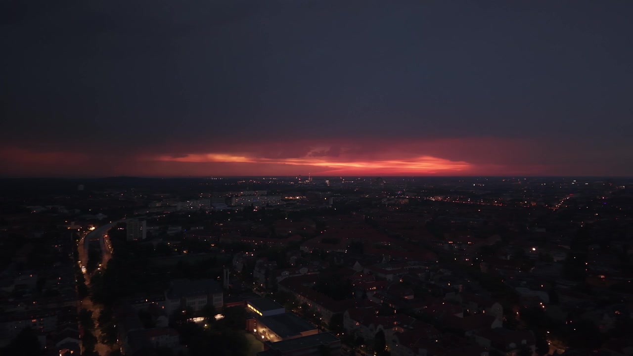Město s viditelným úderem blesku proti bouřkové obloze, osvětlující městskou krajinu v noci. Panoramatický záběr dronem s otáčením doprava.