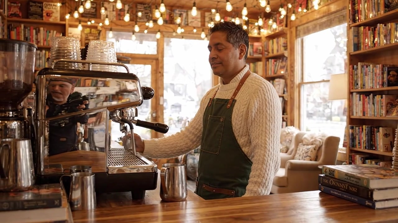 Barista al lavoro: prepara caffè in un accogliente caffè-libreria con luci calde e un'atmosfera invitante, perfetto sia per i lettori che per gli amanti del caffè.