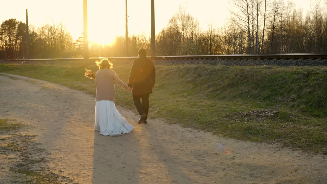 A couple walks hand-in-hand at sunset after their wedding, with soft sunlight glowing