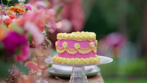 close up pink decorated cake behind colorful flowers at outdoor party, 4k