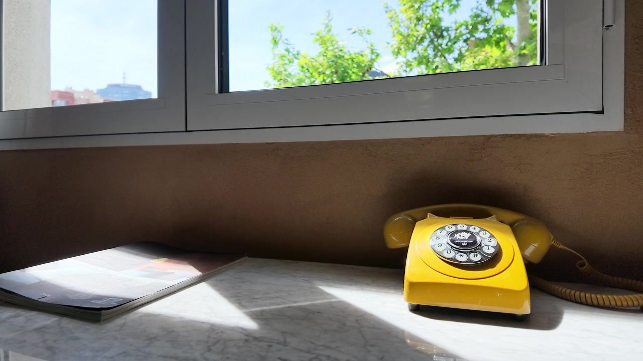 Static shot of a retro yellow telephone on a marble desk under bright natural sunlight