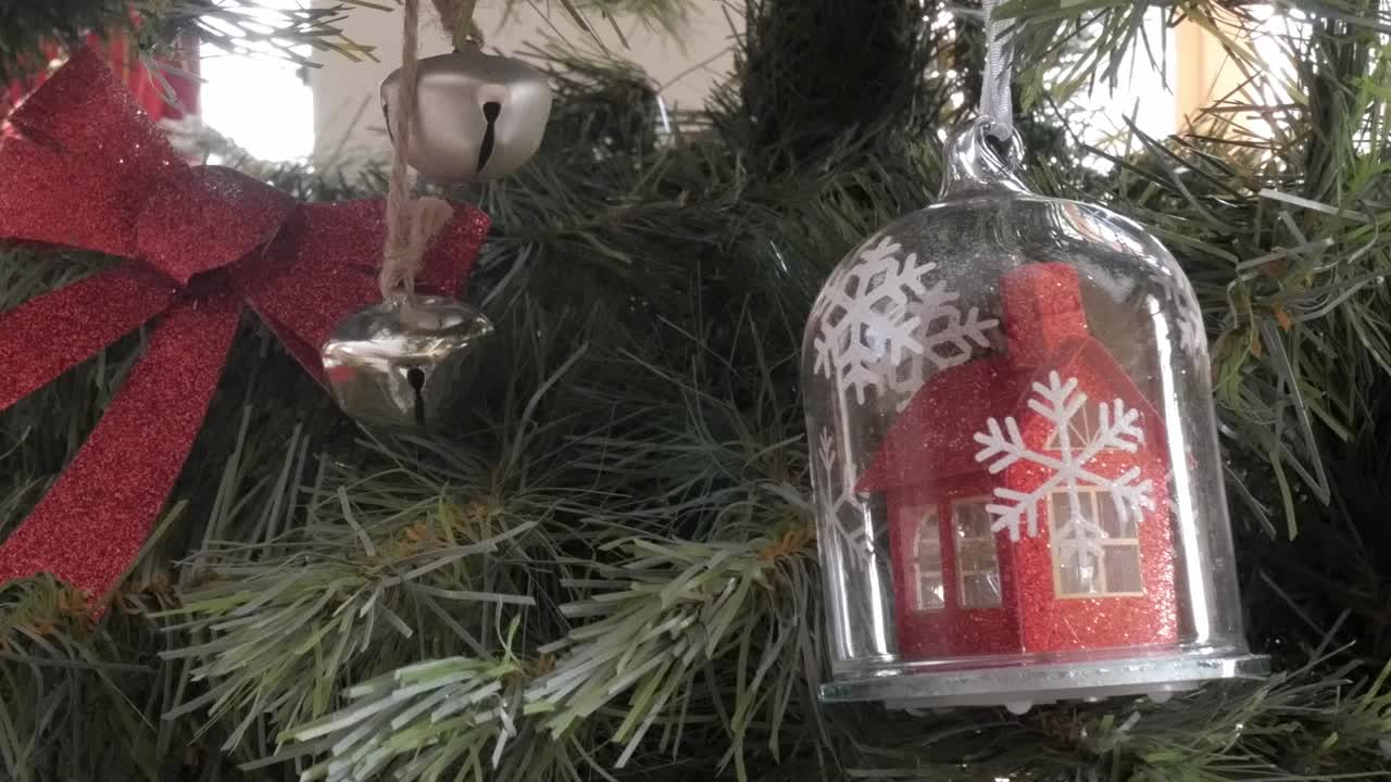 A red house ornament under a glass dome with snowflakes on a decorated Christmas tree
