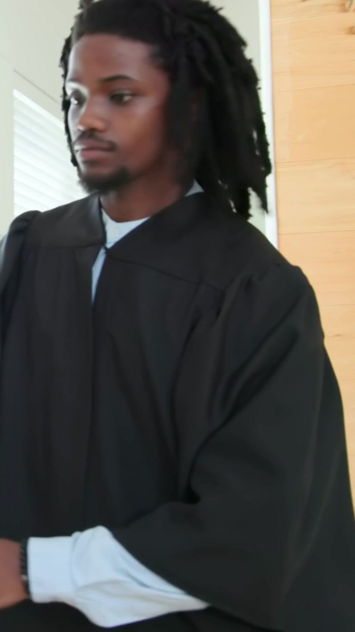 Video verticale: Uomo in tunica nera che si sistema i capelli a casa, camminando con un tocco per un evento.