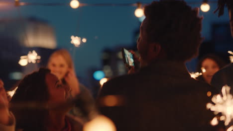 cheerful group of friends holding sparklers celebrating new years eve on rooftop at night having fun dancing enjoying holiday party celebration diverse young people waving festive fireworks