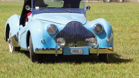 classic blue car driving across grass field