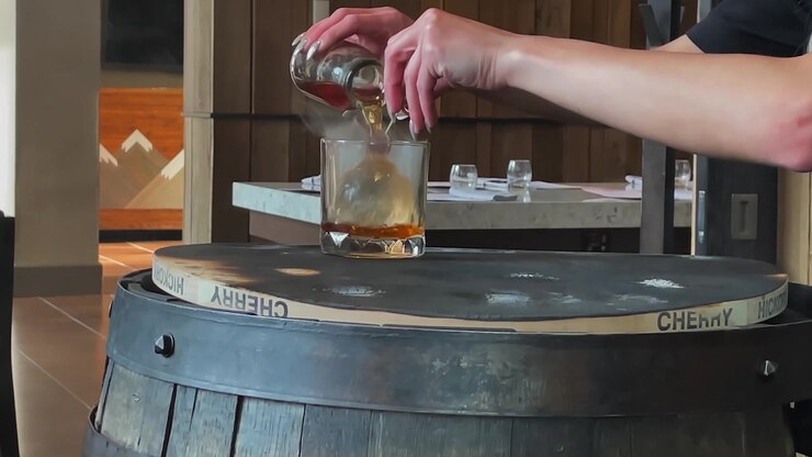 Gylden whisky hældt i et bar-glas med kirsebærrøg og en rund isterning