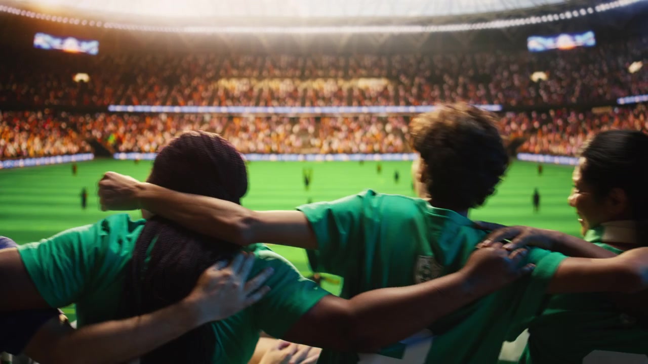 Primer plano de aficionados al fútbol cantando con los brazos entrelazados.