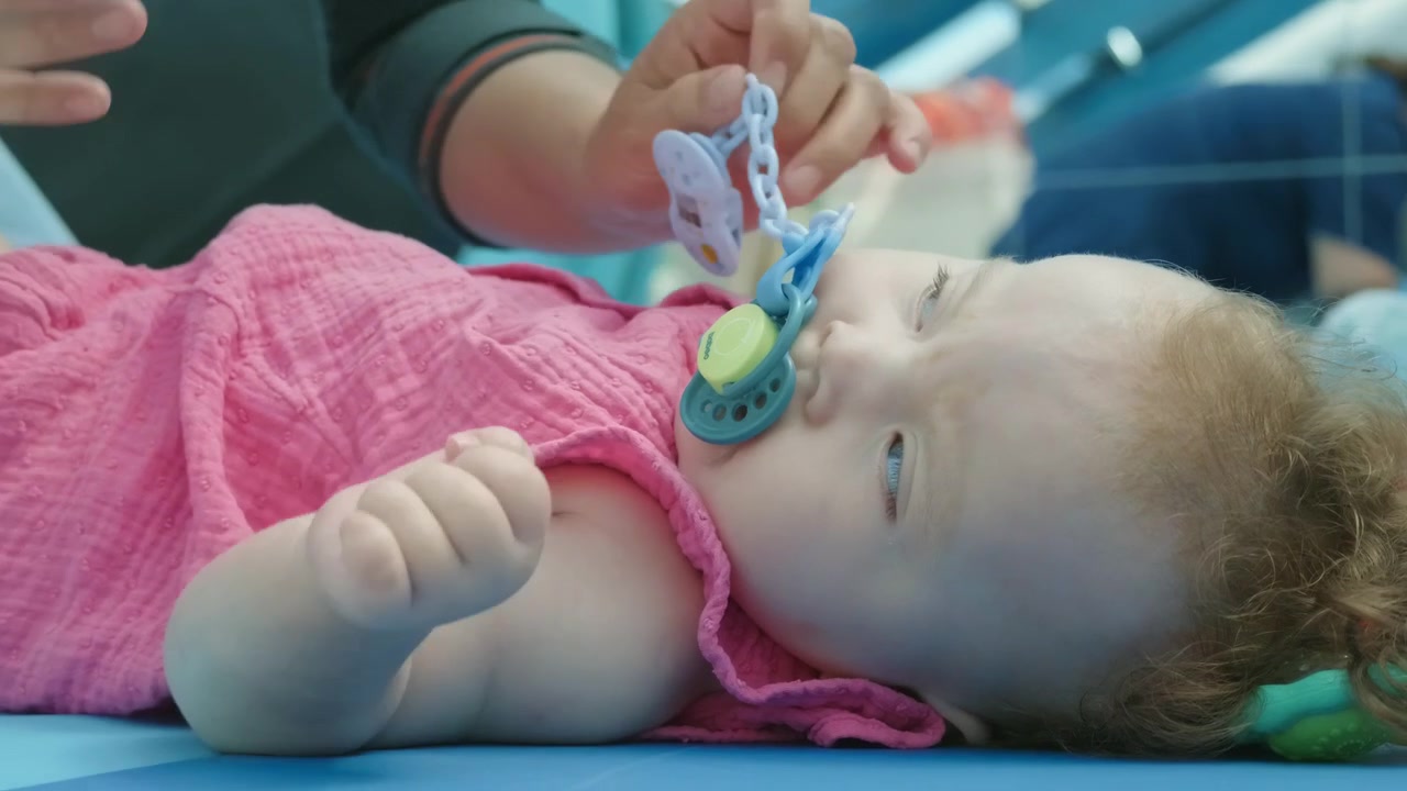 Close-up of a baby girl's face resting on a play mat with a pacifier