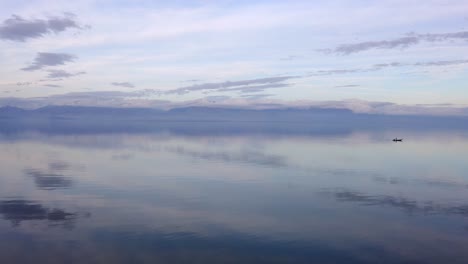 isolated fisherman boat in silent waters of lake reflecting the cloudy sky and small island in middle