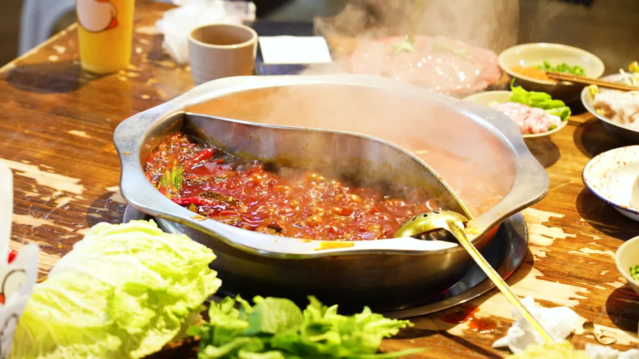 Slow-motion close-up of a traditional Chongqing Sichuan hotpot in a restaurant, showcasing bubbling spicy broth, fresh ingredients, and the vibrant dining experience of Chinese cuisine.