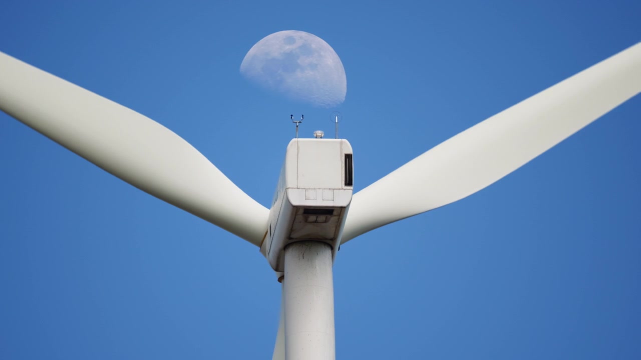 En vindturbin står høyt med bladene roterende mens månen stiger i bakgrunnen. Ideell for prosjekter om bærekraftig energi eller miljødokumentarer