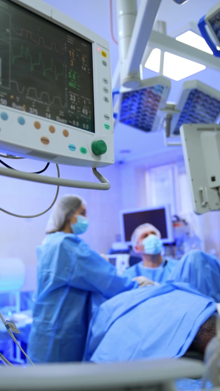 Medico uomo e infermiera strumentista donna eseguono un intervento chirurgico. Il monitor del ventilatore polmonare mostra i segni vitali del paziente. Video verticale.